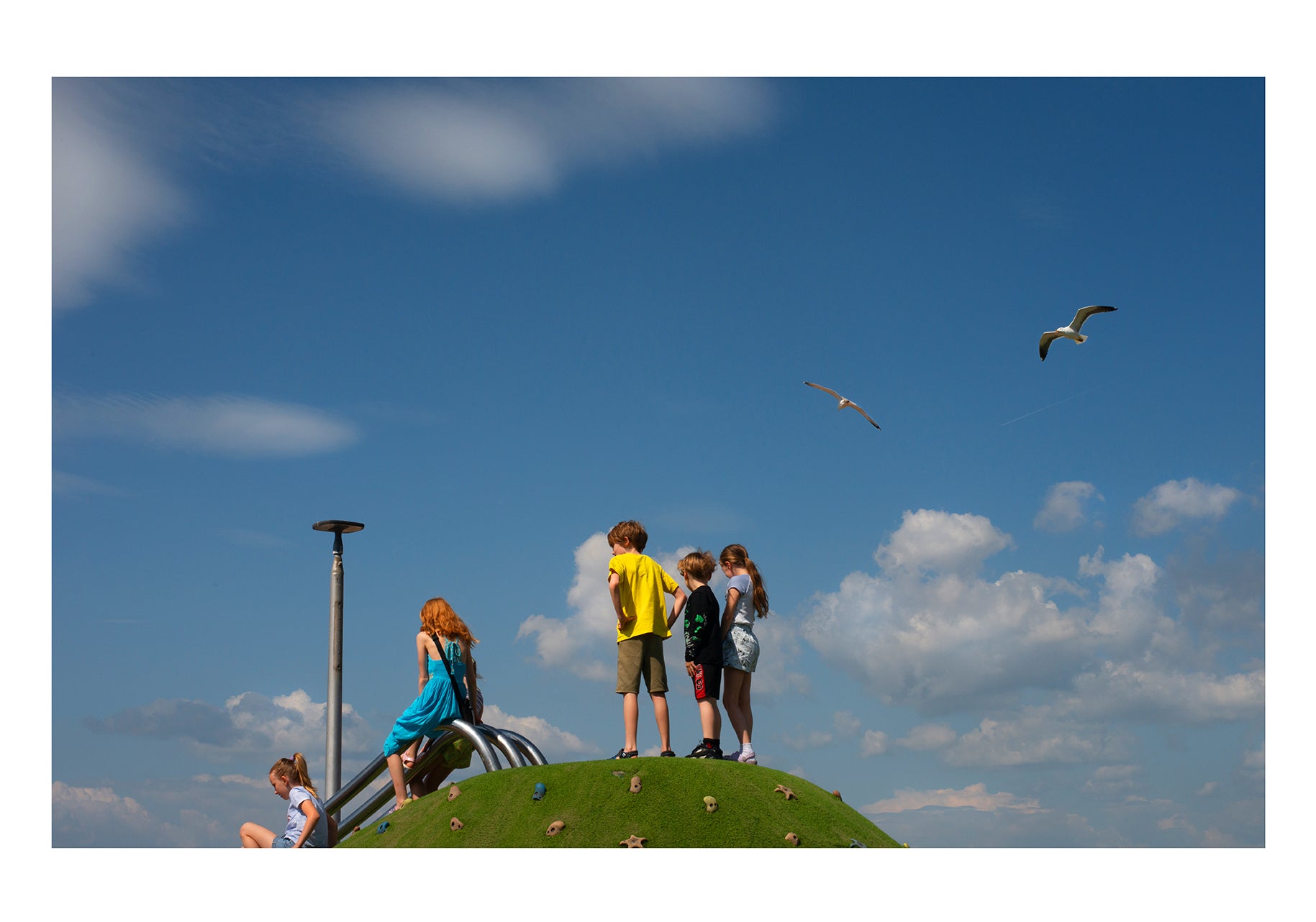 Kids on rounded hill, clouds and seagulls